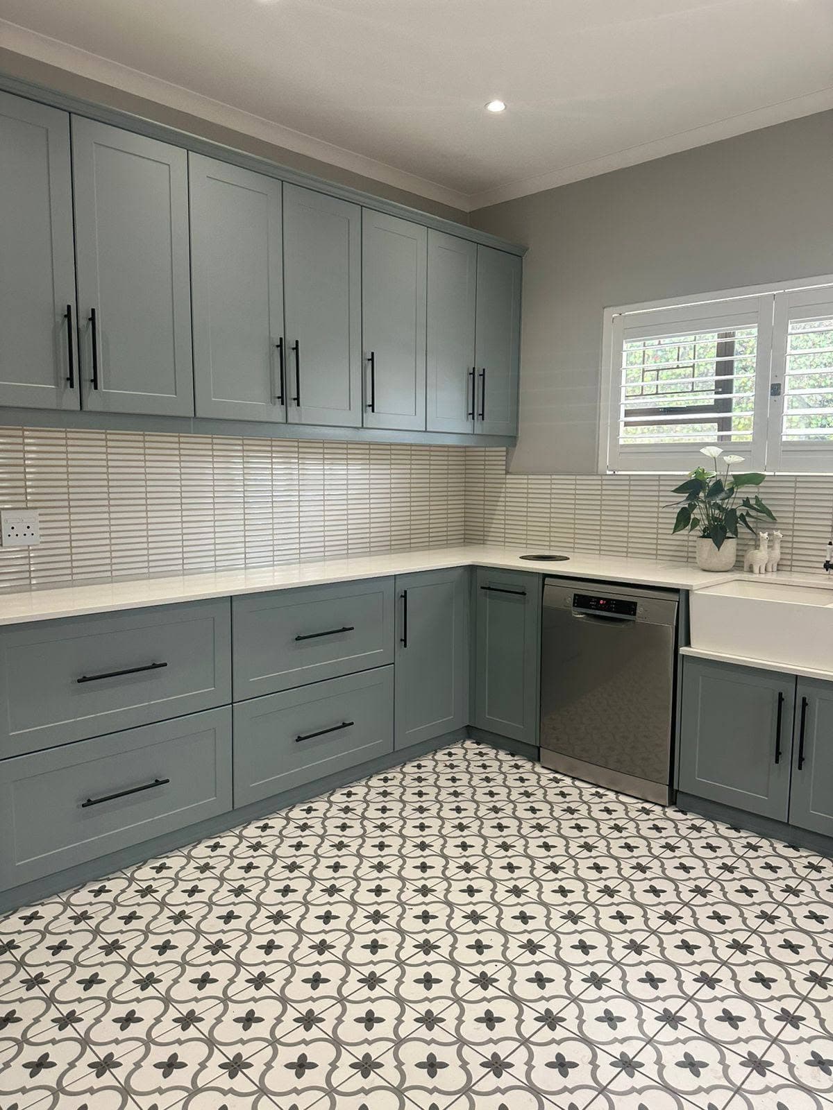 Grey corner kitchen cabinets with white worktops and patterned floor tiles