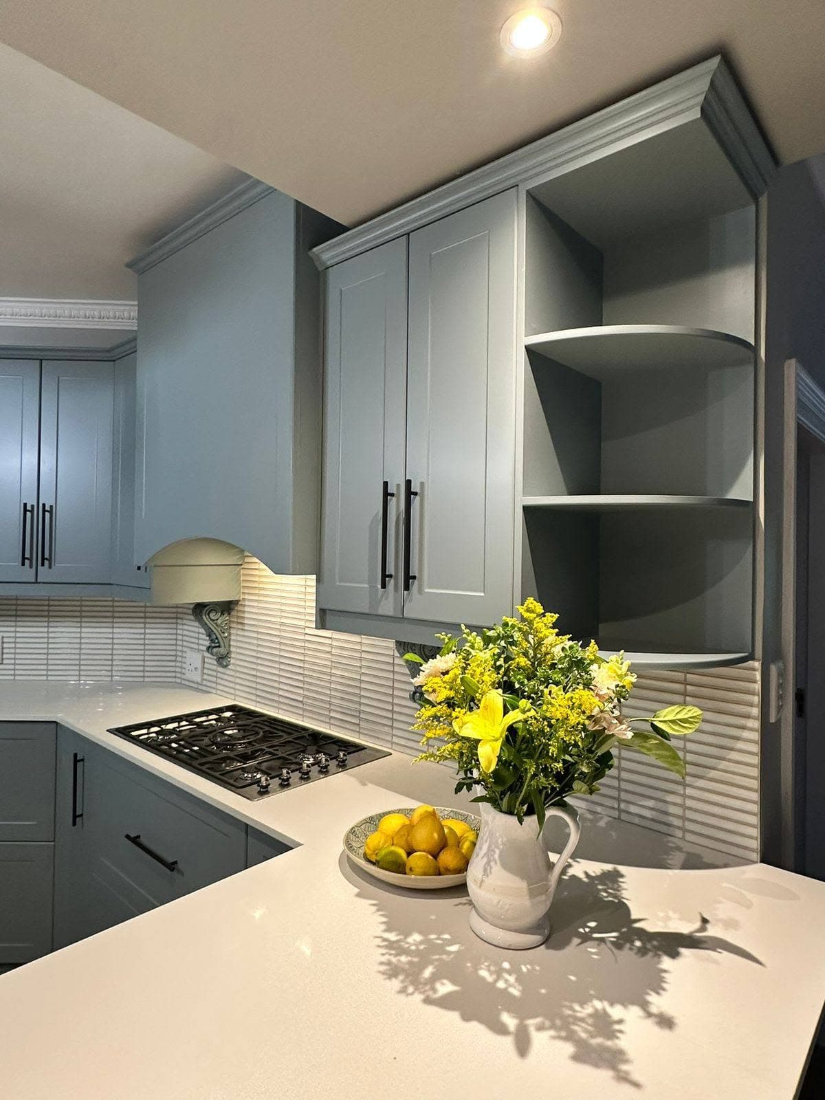 Grey kitchen cabinetry with curved display shelves and a gas hob